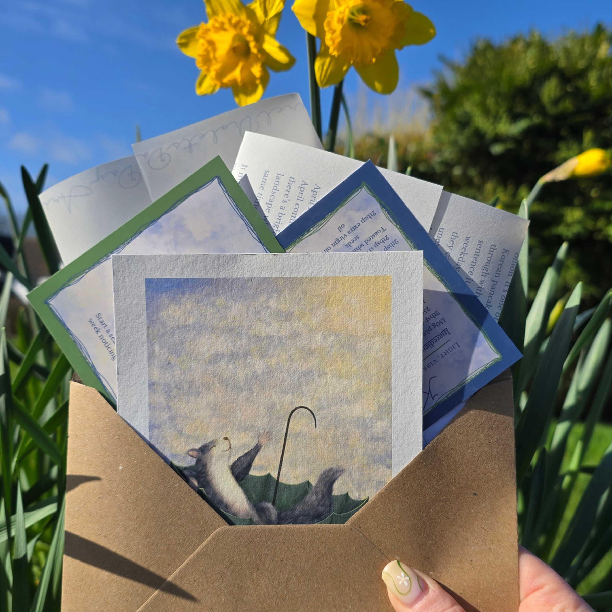 Set of greeting cards with a brown envelope held by a hand, surrounded by daffodils.