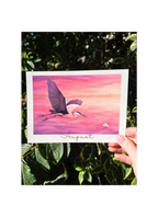 Hand holding a card with a bird illustration and 'August' text against a pink and purple gradient background.