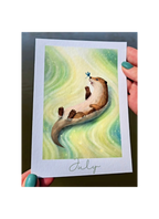 Illustration of an otter holding a dragonfly on a card held by hands with green nail polish.