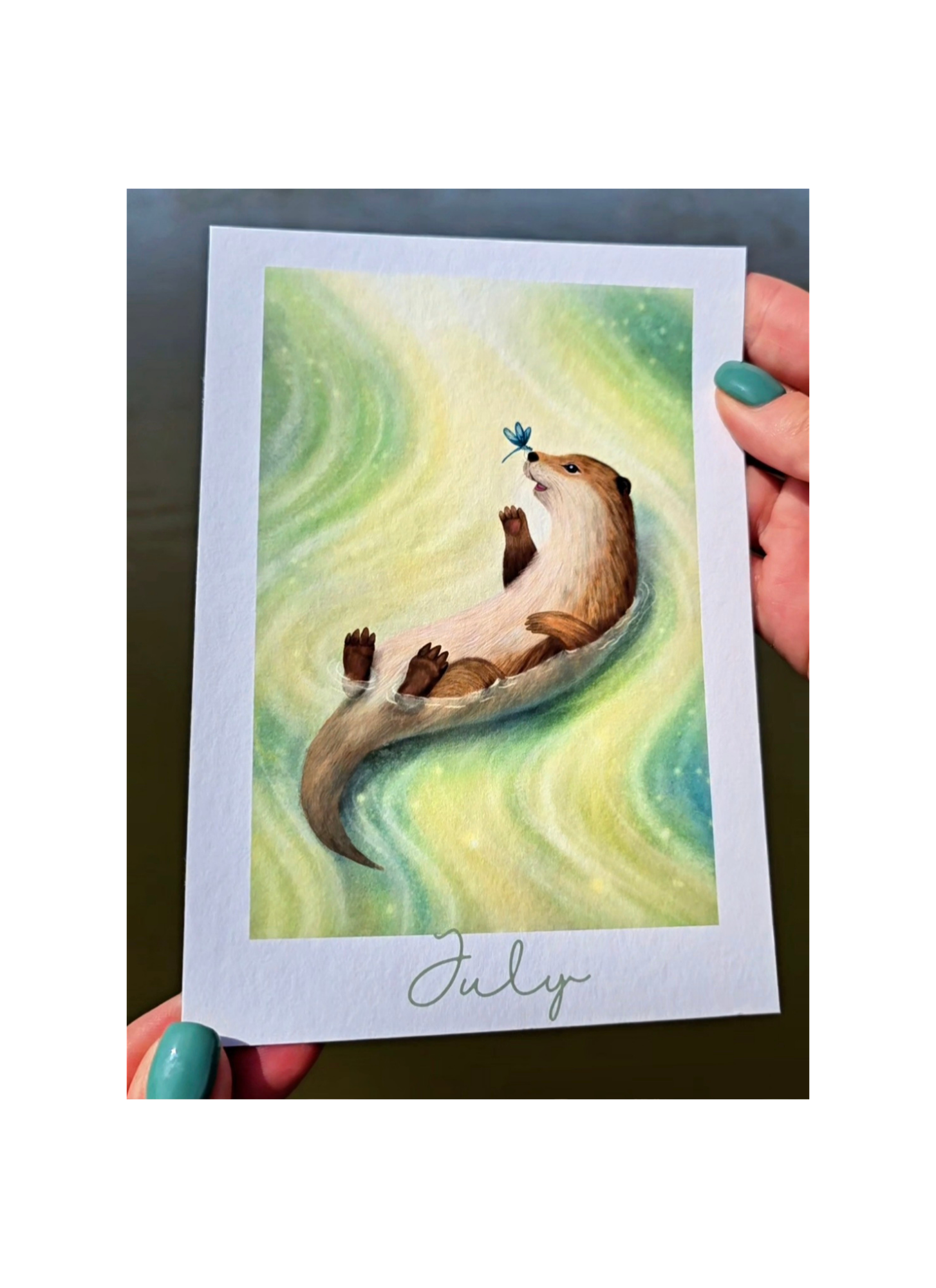 Illustration of an otter holding a dragonfly on a card held by hands with green nail polish.