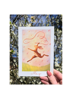 Card with a pink hare illustration and 'May' text held in front of a blurred natural background