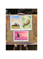 Three colorful paintings on a wooden easel outdoors.