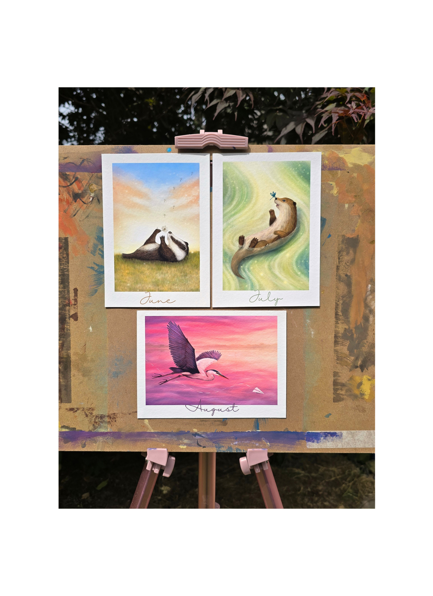 Three colorful paintings on a wooden easel outdoors.