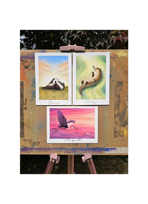 Three colorful paintings on a wooden easel outdoors.