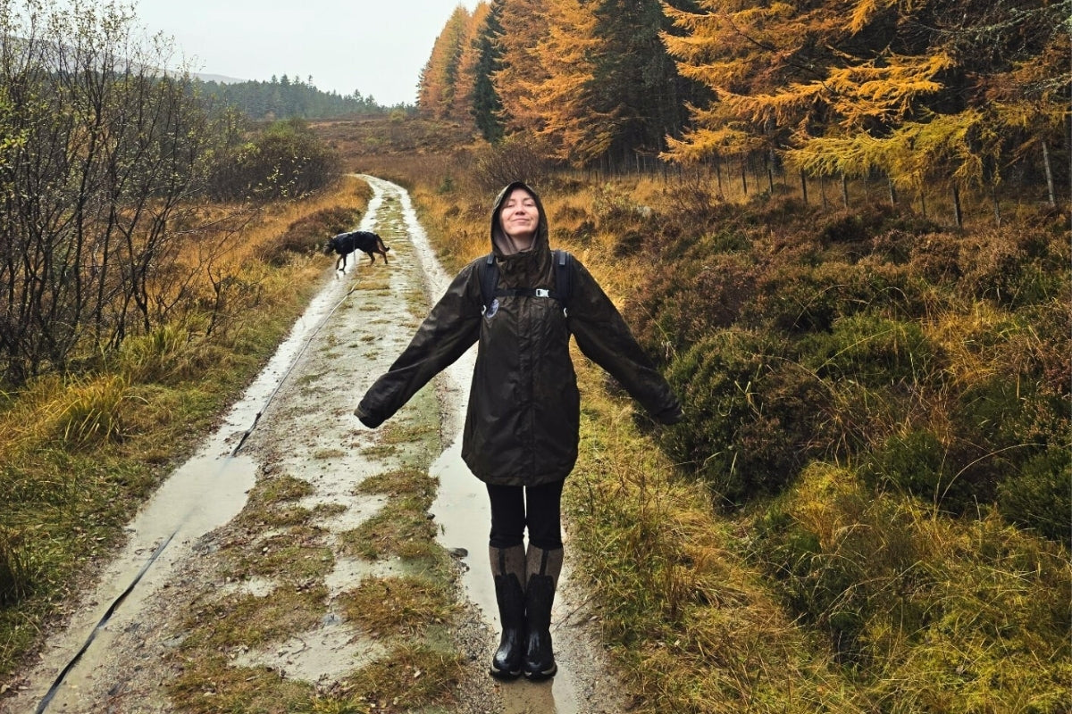 Person in a black raincoat standing on a wet path in a forest with autumn foliage